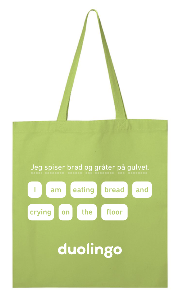 Photograph of a green canvas bag with the Duolingo logo and the silly sentence about eating bread and crying on the floor.