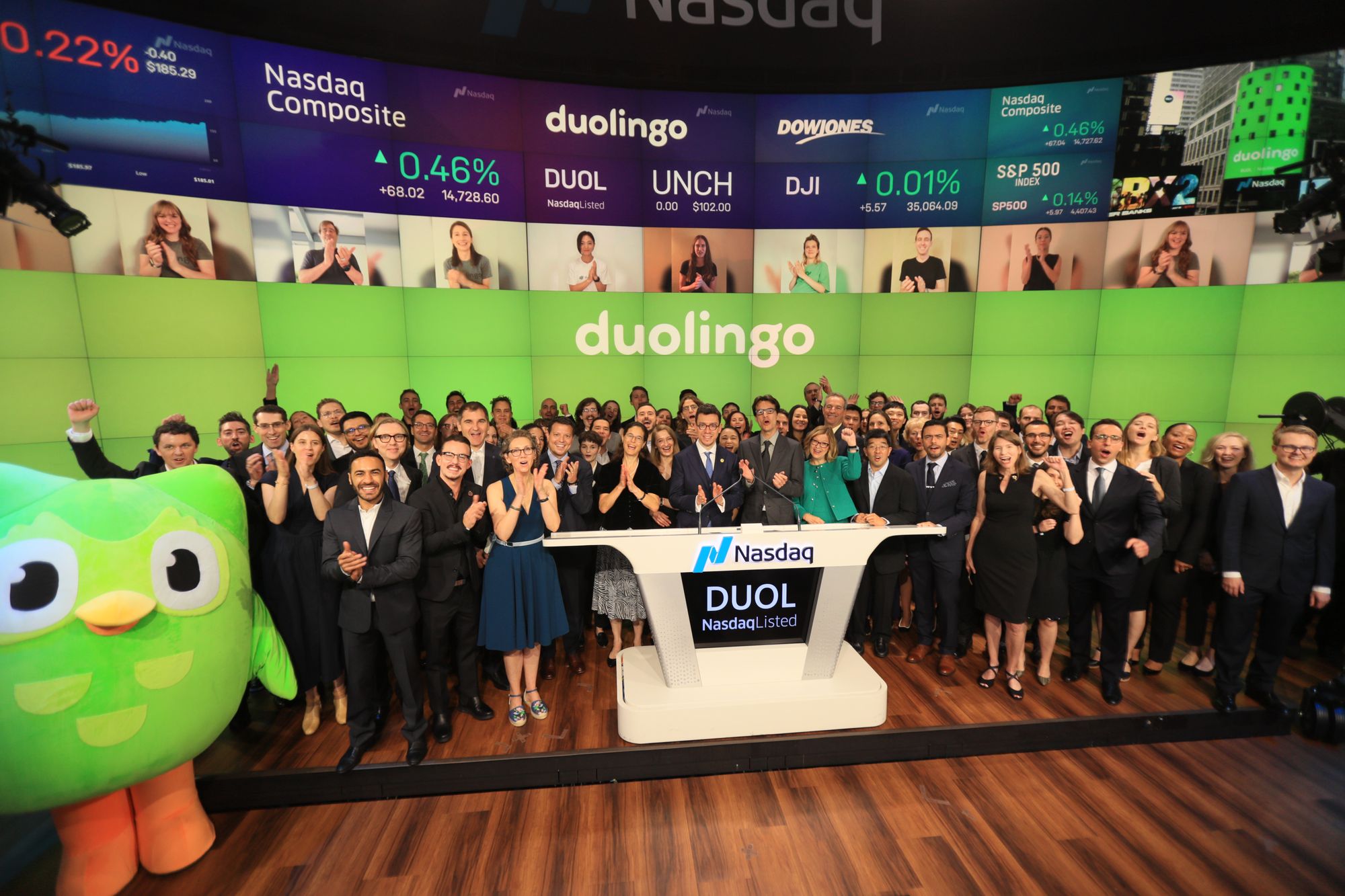 una fotografía del autor del artículo de blog y el cofundador y CEO de Duolingo, Luis von Ahn, de pie con un grupo de alrededor 100 empleados de Duolingo y la mascota de Duolingo, el buho verde, al podio Nasdaq que lleva el símbolo "DUOL".