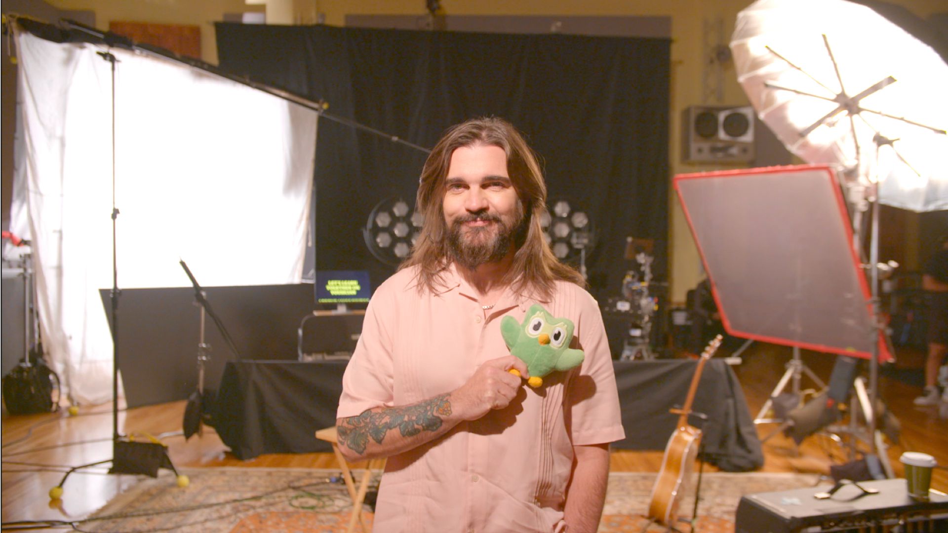 Musician Juanes holding a Duolingo owl plushie in the recording studio