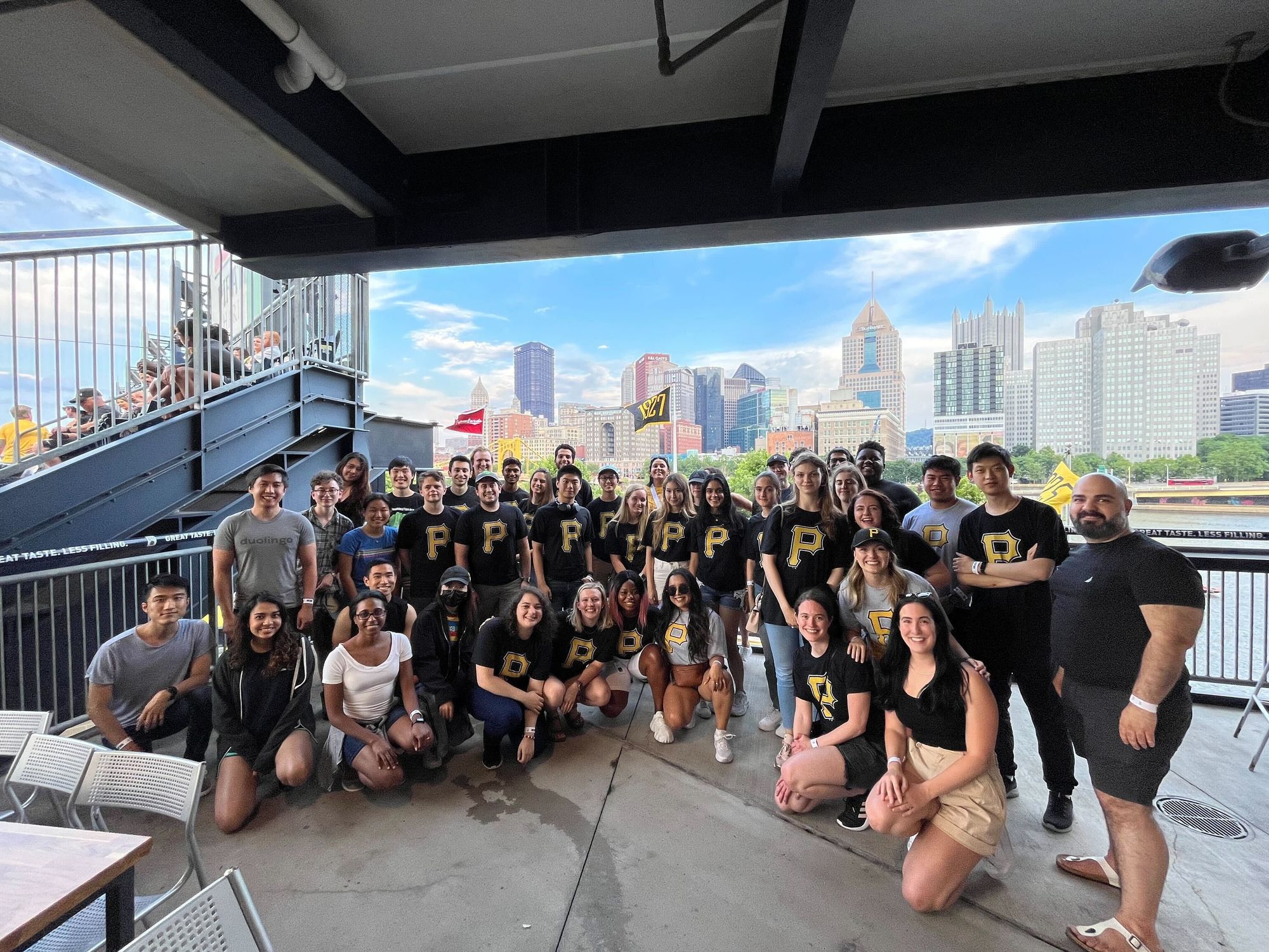 A large group of Duolingo interns in matching t-shirts at a baseball stadium for a Pittsburgh Pirates game