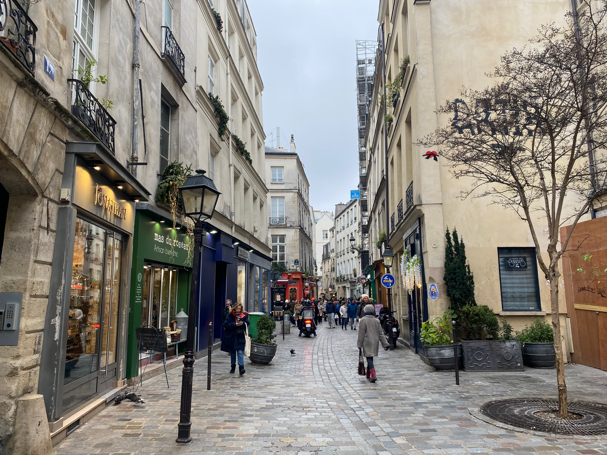 A group of people walking down Rues des Rosiers surrounded by black lamp posts and colorful storefronts. Photo Credit: Justine Hagard