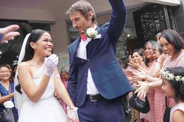 Rob, in a wedding suit, and Amanda, in a wedding dress, laugh and smile for the camera