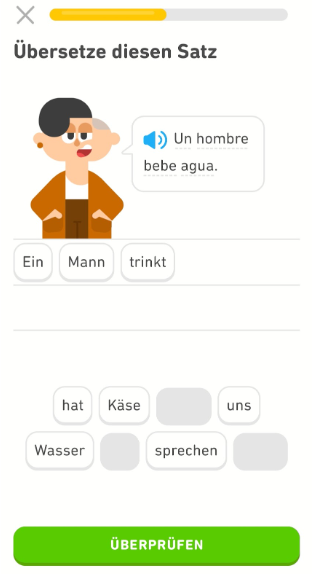 Screenshot einer Übung mit dem spanischen Satz „Un hombre bebe agua.“ Die deutsche Übersetzung darunter wird in Form von Wortkacheln dargestellt, die zusammen „Ein Mann trinkt Wasser“ ergeben.