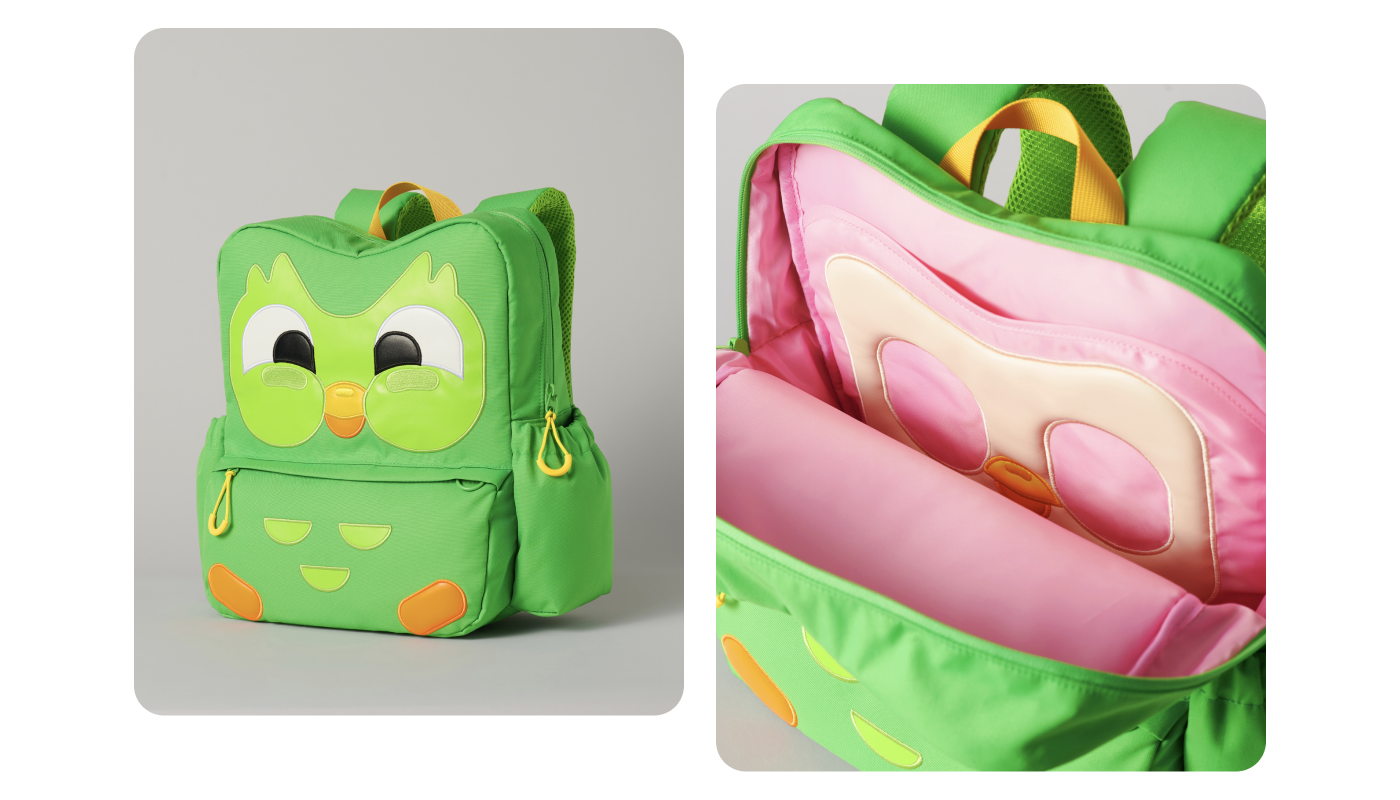 A lime green backpack that is made to look like Duo the owl. On the front pouch of the backpack you can see his three chest feathers as well as his orange feet. His smiling eyes and beak adorn the main portion of the backpack. There is a compartment for a water bottle as well. Inside, the back reveals a pink interior with the suggestion of Duo’s skeleton sewn onto the inner laptop sleeve compartment.