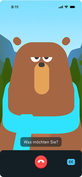 Screenshot of a video call with Falstaff. Falstaff the bear is facing the user with a serious expression on his face. The caption below displays a question in German, “Was möchten Sie?” At the bottom of the screen is a red icon with an image of a phone, indicating the option to end the call. To the right is a blue rectangle with the letters “CC” inside, indicating the option to show or hide captions.