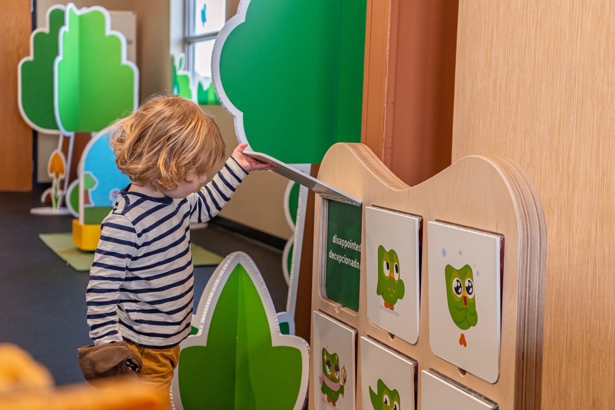 A child at Duo’s Treehouse lifting up a panel on a Duo-themed board with Spanish and English words on it.